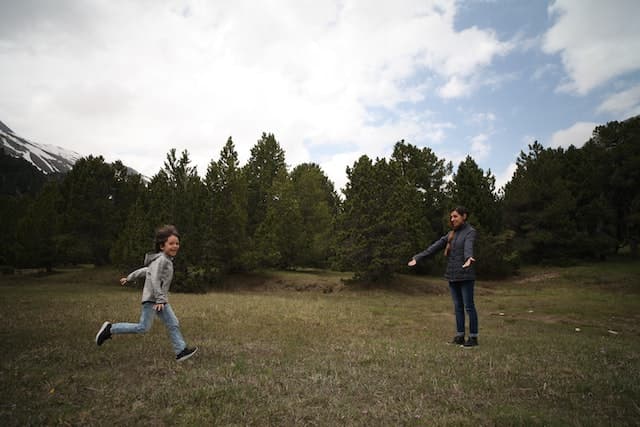 A young boy runs toward his mother, who has her arms outstretched toward him, and a big smile on her face.