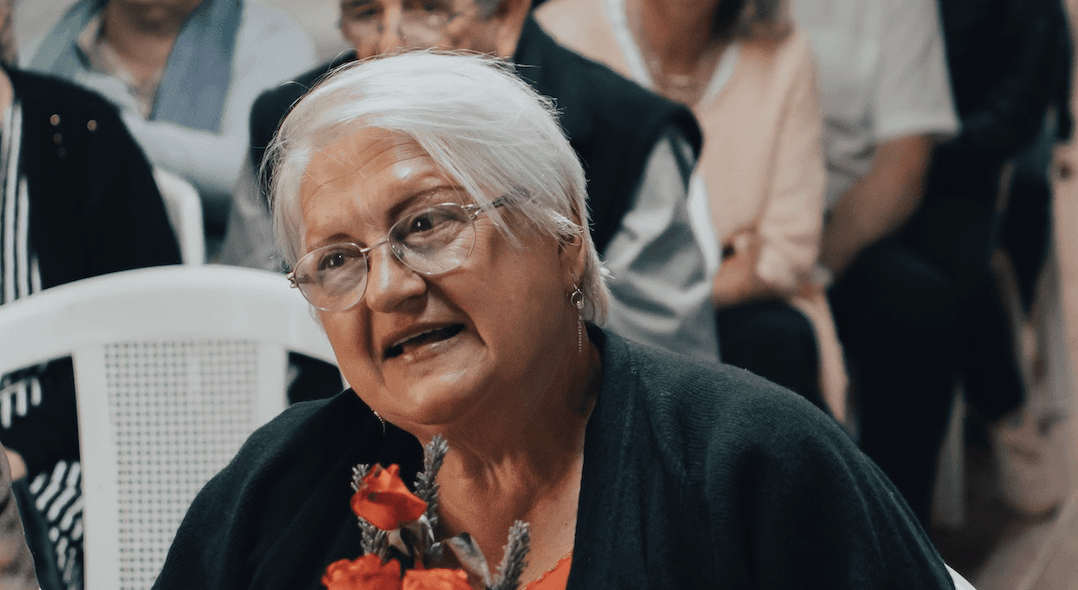 A woman holding flowers speaks at a gathering.