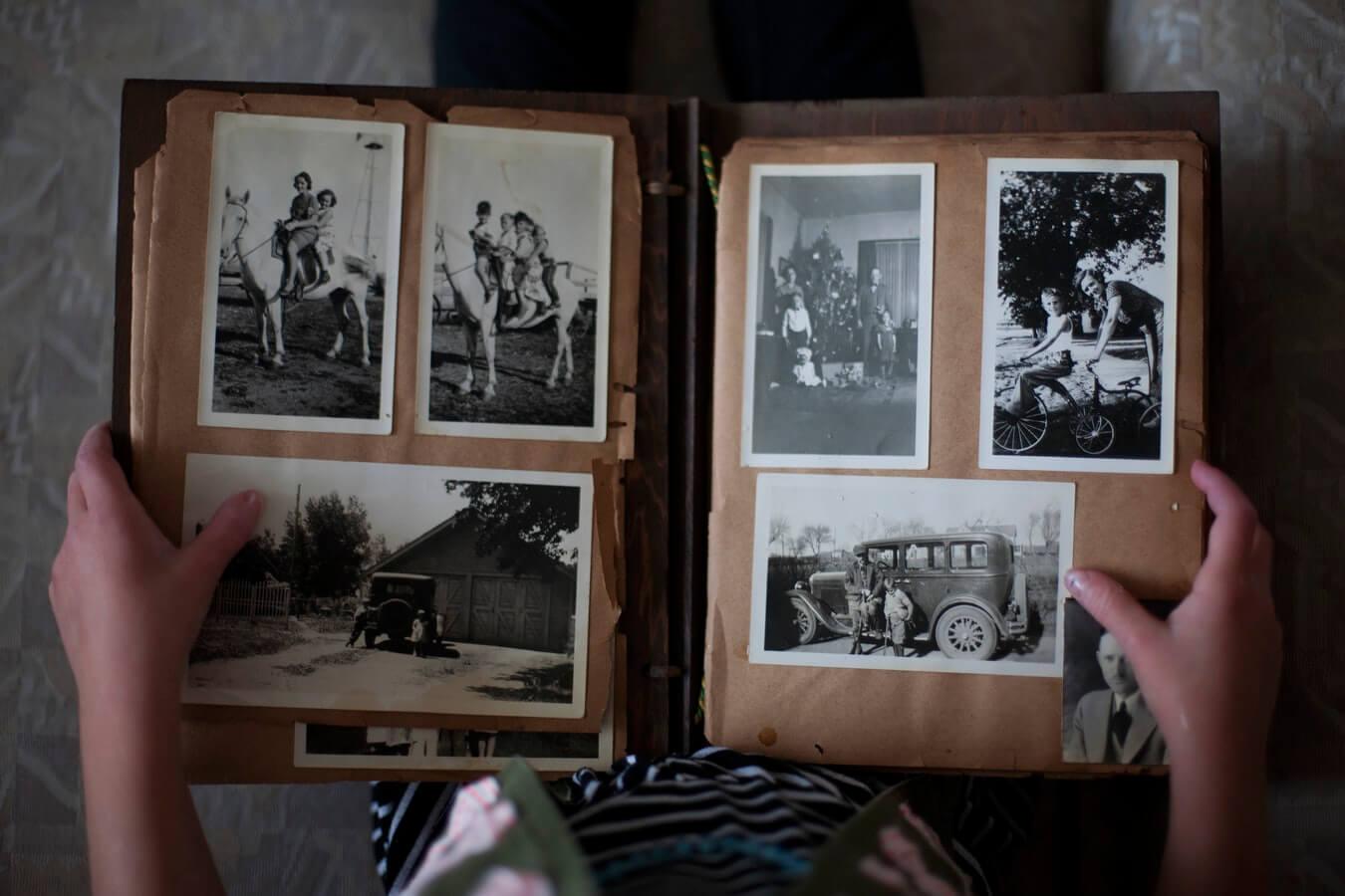 A pair of hands holds a very old photo album containing black-and-white family photos.