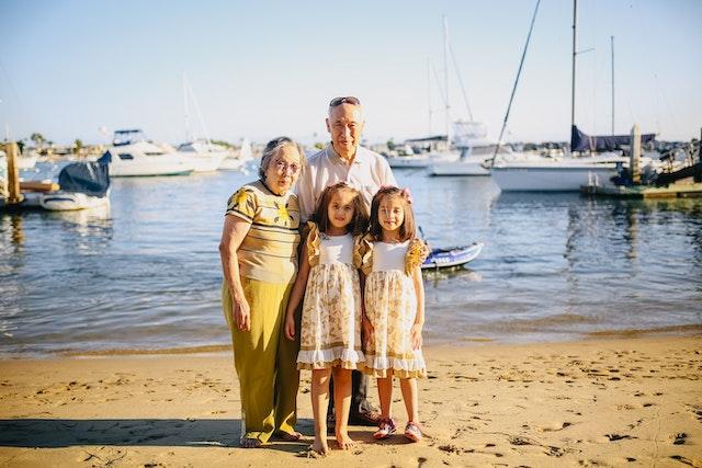 Grandparents pose for a photo with their two granddaughters on the beach at a marina.