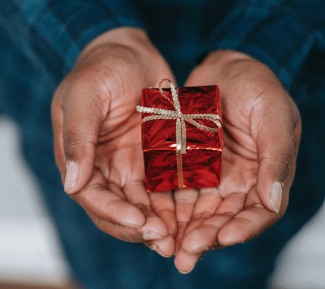 Hands cup a tiny gift, wrapped in red paper with a small gold ribbon.
